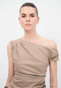 Asymetrické šaty na jedno rameno v světlém odstínu tan, elastické látce s jemným drapováním, s decentní strukturou a přiléhavým střihem.