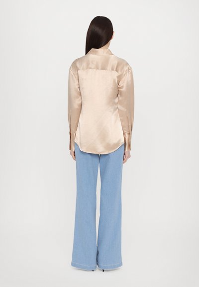 Satin long-sleeve shirt in light beige with a collared neckline and a curved hem, paired with wide-leg blue jeans.