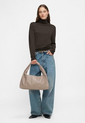 Jasno beżowa skórzana torebka o luźnym fasonie i zaokrąglonym uchwycie; zestawiona z ciemnym długim topem i niebieskimi spodniami typu wide-leg.
