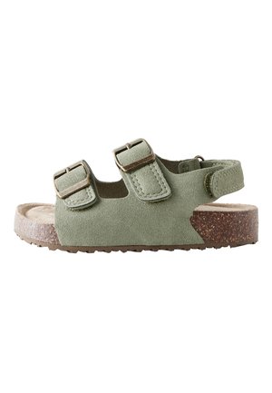 Grøn ruskindssandal med to justerbare spænder på toppen og en rem med velcro ved hælen, med korksål og tekstureret bund.