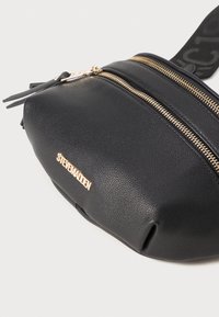 Black leather fanny pack with a textured finish, dual gold zip closures, and a gold logo accent. Features a fabric strap with a logo pattern.