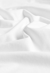 Tissu blanc doux avec une texture de tissage fine visible, légèrement froissé et plié en courbes irrégulières et lisses.