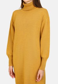 Abito maglione a maniche lunghe, color giallo senape, realizzato in tessuto lavorato a maglia; presenta polsini a coste e una vestibilità comoda.