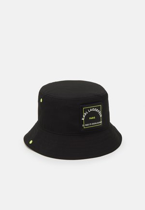 Zwarte bucket hat met neon groene oogjes en een voorop geplakte patch met de tekst "Karl Lagerfeld Paris 21 Rue St-Guillaume."