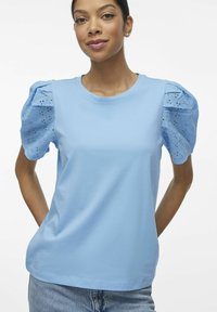 Jasnoniebieska koszulka z krótkim rękawem typu puff, wykonana z materiału w dziurkowany wzór. Okrągły dekolt, miękka tekstura, dopasowany krój i gładkie wykończenie.