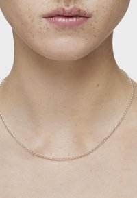 Collar de cadena de plata con un delicado diseño de eslabones redondos, reposando en la piel del cuello, mostrando una textura suave y un brillo. 