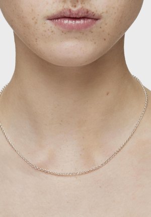 Collar de cadena de plata con un delicado diseño de eslabones redondos, reposando en la piel del cuello, mostrando una textura suave y un brillo.