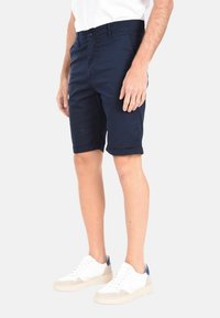 Pantaloni corti blu navy realizzati in tessuto liscio, con una vestibilità dritta e orlo arrotolato. Abbinati a sneakers bianche e una maglietta bianca.