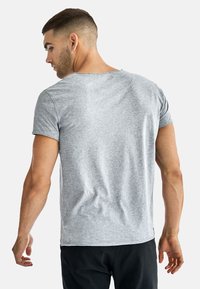 Grå kortärmad t-shirt med rund halsringning, mjuk textur och en svag kurva vid fållen, sedd bakifrån.
