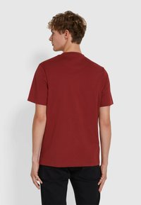 T-shirt di cotone rosso con maniche corte, colletto a giro e orlo dritto. Indossata da una persona di spalle su uno sfondo neutro.
