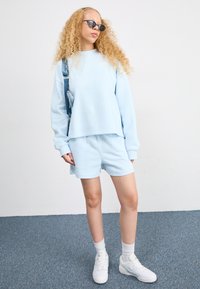 Helles blaues Sweatshirt und passende Shorts aus weichem Material, mit lockerer Passform. Getragen mit weißen Sneakern und lässigen weißen Crew-Socken.