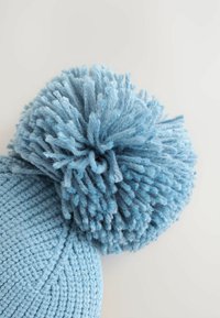 Cappello in maglia blu con un grande pon-pon testurizzato sulla parte superiore. Il materiale è morbido, con un design a coste e una superficie liscia.