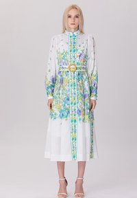 Robe midi fleurie en tissu léger, avec des motifs bleus et jaunes, des manches longues, un col montant et une large ceinture avec une boucle circulaire.