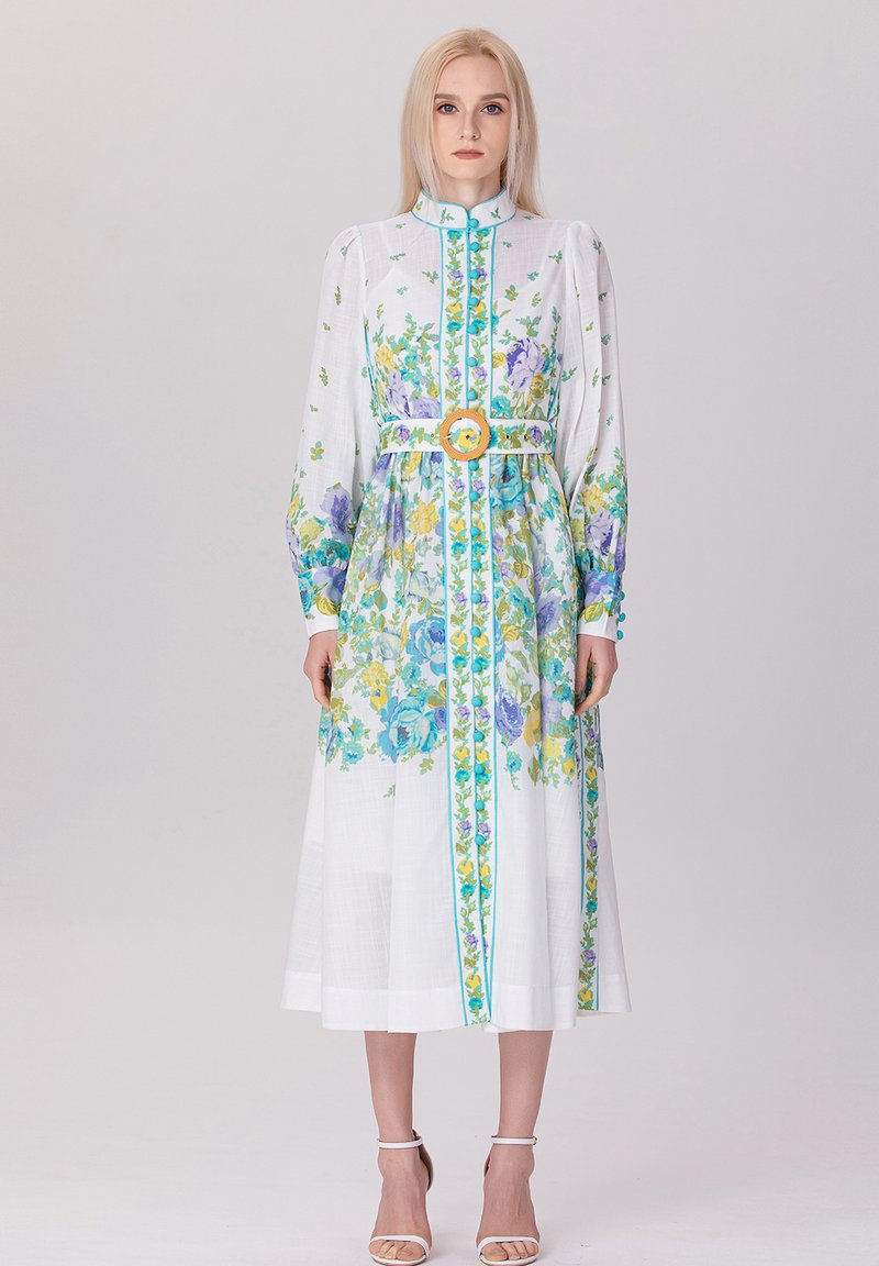 Robe midi fleurie en tissu léger, avec des motifs bleus et jaunes, des manches longues, un col montant et une large ceinture avec une boucle circulaire.