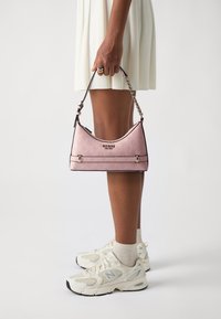 Borsa a spalla rosa con un motivo in rilievo e bordi neri, dotata di un logo argentato e di una tracolla a catena. Indossata con sneakers bianche casual.