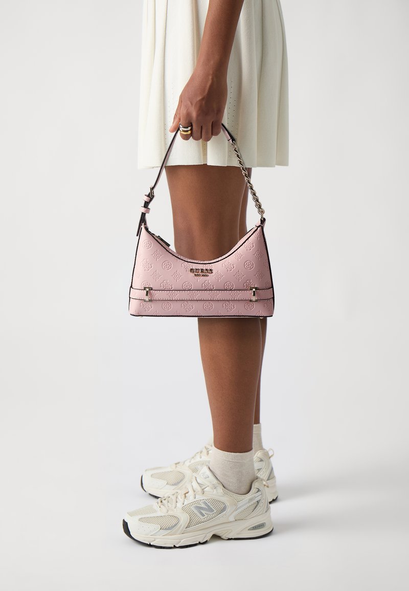 Borsa a spalla rosa con un motivo in rilievo e bordi neri, dotata di un logo argentato e di una tracolla a catena. Indossata con sneakers bianche casual.