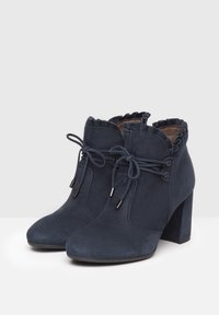 Botines de ante azul marino con un cuello festoneado, cordones y un tacón grueso. Presentan material texturizado y acentos metálicos.