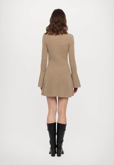 Rochie bej tricotată, ajustată, până la genunchi, cu mâneci lungi tip clopot. Pur și cu cizme negre până la genunchi, având o textură netedă și o formă bine definită.