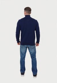 Marineblaues, gestricktes Oberteil mit hohem Kragen, getragen über hellblauen Jeans, mit schlanker Passform und gerippten Bündchen und Saum.
