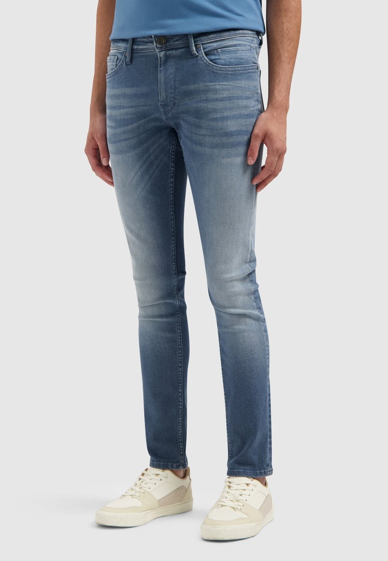 Lichtblauwe spijkerbroek met een slim fit, vervagingdetails, vijf zakken en een knoopsluiting, in combinatie met crèmekleurige sneakers.