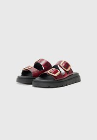 Røde sandaler med slangebåndmønster, slip-on design, to justerbare guldbukler, sort gummisål og åben tå. Tekstureret overflade.