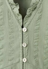 Jasnozielona bluzka z materiału z falbanowym dekoltem, pionowymi teksturowanymi paseczkami i okrągłymi, perłowymi guzikami z przodu.