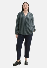 Bluză cu mânecă lungă, decolteu în V, în nuanță de teal închis, cu dungi verticale și detalii pliate, asortată cu pantaloni navy croiți și mocasini negri.
