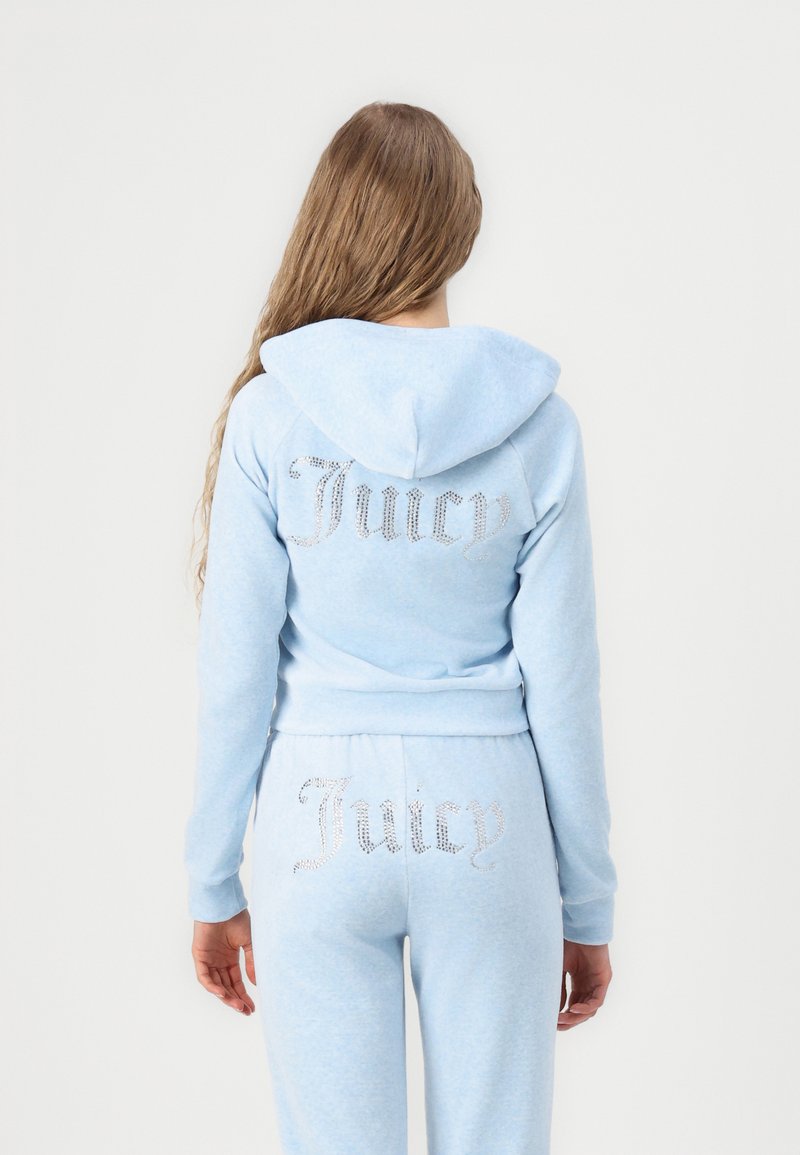Lichtblauwe velours trainingspak met een aansluitende sweatshirt met capuchon. "Juicy" in strasssteentjes op de achterkant, bijpassende broek met "Juicy" op de achterkant.