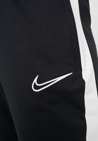 Nahaufnahme von schwarzen Sporthosen mit weißem Seitestreifen und dem weißen Nike-Swoosh-Logo, das in der Nähe der Tasche gestickt ist.