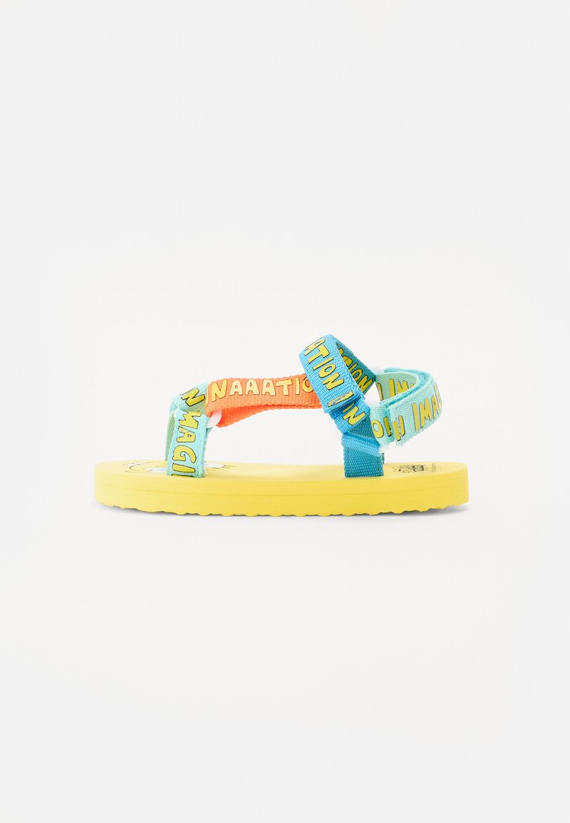 Felle gele sandaal met blauwe en oranje bandjes, voorzien van tekstpatronen. Platte zool met een gestructureerde onderkant voor grip, casual ontwerp.