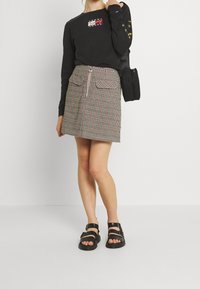 Zwarte lange mouwen shirt met een gekleurde logo, gecombineerd met een geruite mini rok met voorzakken en een zilveren rits. Zwarte sandalen.