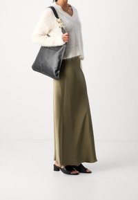Pull blanc moelleux, jupe maxi satin olive, sac en cuir noir avec accessoires dorés, et sandales noires à talon bas.