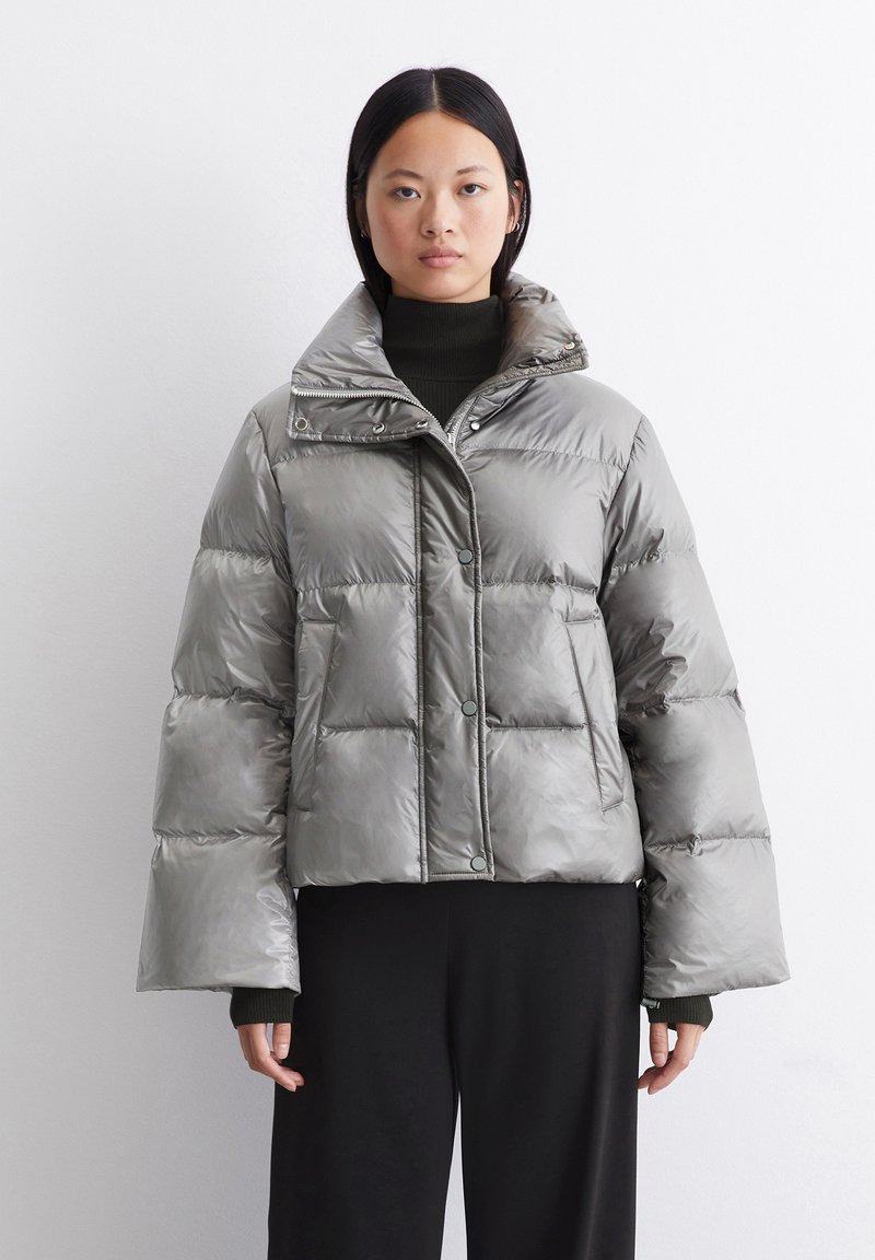 Grå pufferjakke med en cropped design, store puffede seksjoner, høy krage og trykknappslå. Glatt, blank tekstur.