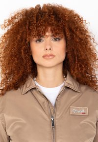 Hellbraune Satinjacke mit Reißverschluss, Stehkragen und Schott-Label auf der linken Brust. Das Model hat lockige rote Haare.