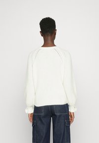 Valkoinen neulottu rento villapaita, jossa raglanhihat ja resorit hihansuissa. Sisältää teksturoidun kankaan ja pehmeän, pörröisen ilmeen.