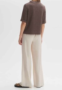 Blusa corta a maniche corte in tono marrone con texture, abbinata a pantaloni a gamba larga color crema chiaro, caratterizzati da una vestibilità comoda e dettagli con risvolti.