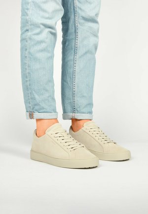 Beige Wildlederschuhe mit runder Zehenpartie, flachen Schnürsenkeln und einem minimalistischen Silhouette. Kombiniert mit hochgekrempelten hellblauen Jeans.