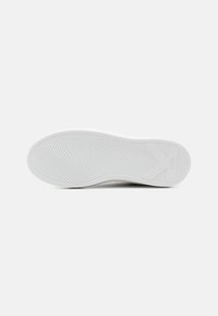 Bijela tenisica s potplatom s teksturiranim, valovitom šablonom i detaljem loga. Glatki gumeni materijal nudi prianjanje i potporu.