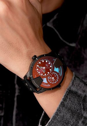 Montre analogique avec un cadran rouge et un boîtier noir. Dispose de plusieurs sous-cadrans et d'accents lumineux. Attache à un bracelet texturé noir.