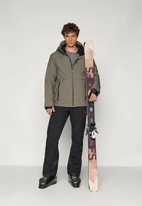 Olive rohelise värvi suusajakk, millel on eesne särgiga tõmblukk, mustad suusapüksid ja mustad saapad. Hoides suuska pruunide ja mustade aktsentidega. Lihtne disain.