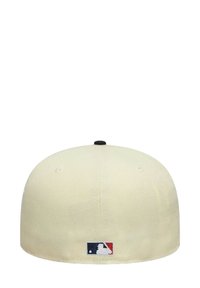 Cream baseball cap with a rounded crown, a black button on top, and an embroidered MLB logo in red, white, and blue at the back.