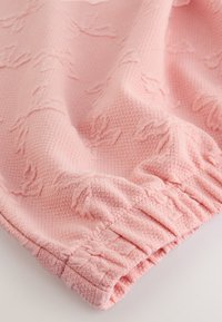 Tessuto rosa pallido con un motivo strutturato, caratterizzato da una vita arricciata e una superficie liscia. Il materiale appare morbido e leggero.