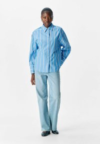 Hellblau gestreifte Button-down-Bluse mit Kragen, kombiniert mit hellblauen Jeans. Das Hemd hat lange Ärmel und eine lässige Passform.