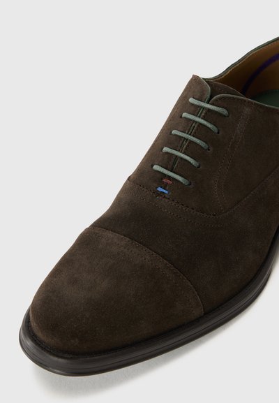 Scarpe da abito in suede marrone con punta arrotondata, lacci verdi e cuciture a contrasto. Suola liscia e superficie superiore testurizzata.