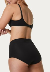 Svart bralette med justerbara remmar och spänne, kombinerad med högmidjade svarta trosor. Slät textur, inga synliga mönster eller detaljer.