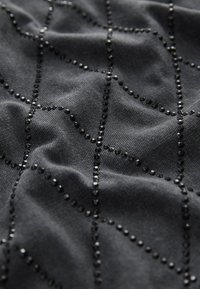 Tessuto nero con una superficie testurizzata che presenta un motivo geometrico creato da piccoli perline nere lucide disposte in linee.
