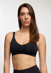 Brassiere wireless nero con una texture liscia, design a V e spalline larghe. Il tessuto appare morbido con cuciture minime per un aspetto pulito.