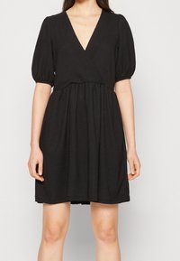 Vestido corto negro con un profundo escote en V, mangas abullonadas y cintura fruncida. Hecho de una tela texturizada, hasta la rodilla y con un corte relajado.