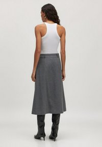 Grauer Wollrock mit gerader Silhouette und Taillenbund, kombiniert mit knielangen schwarzen Stiefeln und einem figurschmeichelnden weißen Tanktop.