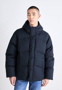 Mörk marinblå vadderad jacka med hög krage och huva, med en texturerad, quiltad design och dragkedja framtill.